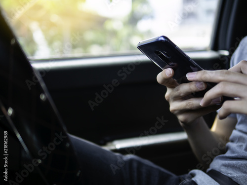 Driver holding mobile, use phone while stopping. Smart phone concept, browsing, call, typing, texting, searching or internet connection. Steering wheel interior right-hand drive car in background.