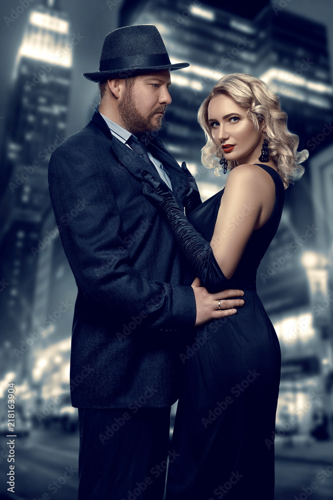Film noir. Detective man in a raincoat and hat and a dangerous woman with  red lips in black dress. Couple stands against the background of the night  city Stock Photo | Adobe