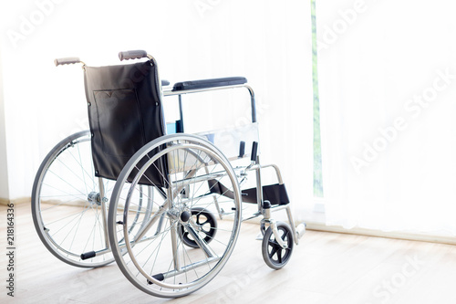 A wheelchair is parking at hospital room or house near curtain and window in the evening with copy space. Wheelchair suit for old people, disabled, patient. It’s important and useful thing for them.