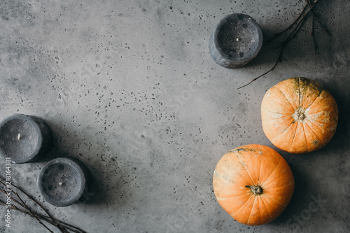 Halloween background, still life flat lay composition of black candles, small pumpkins, dried branches over grey. Top view, place for text.