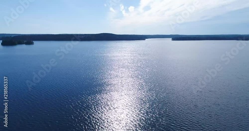 Aerial - Drone flying forward above lake and water. Clear and sunny summer day, calm waves and sun light reflections. Kangasala Finland photo