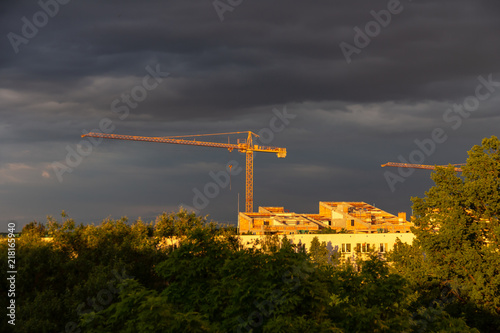A construction crane standing by an unfinished building illuminated by the rays of the setting sun
