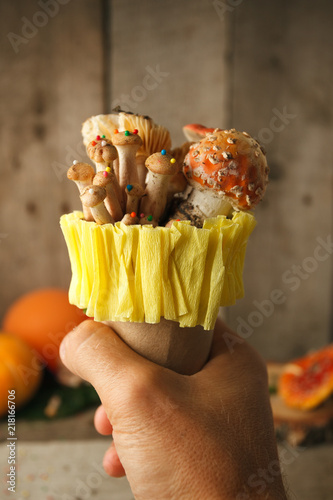 fantastic ice cream with candy mashroom in hand on wooden background, concept of poisin, nagic food, halloween holiday funny food photo