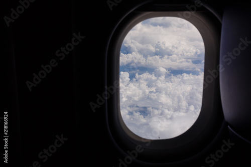 Plane window view with blue sky and clouds.