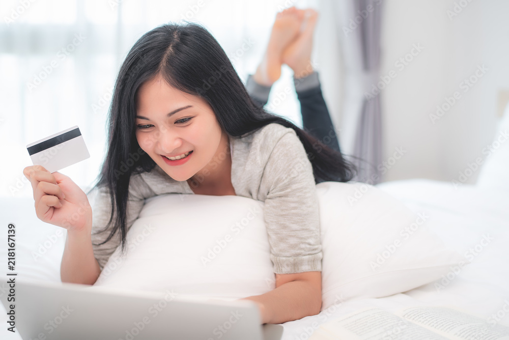 Pretty attractive Asian woman shopping online by laptop with credit card, laying on the bed at bedroom Pretty attractive Asian woman shopping online by laptop with credit card, laying on the bed at bedroom