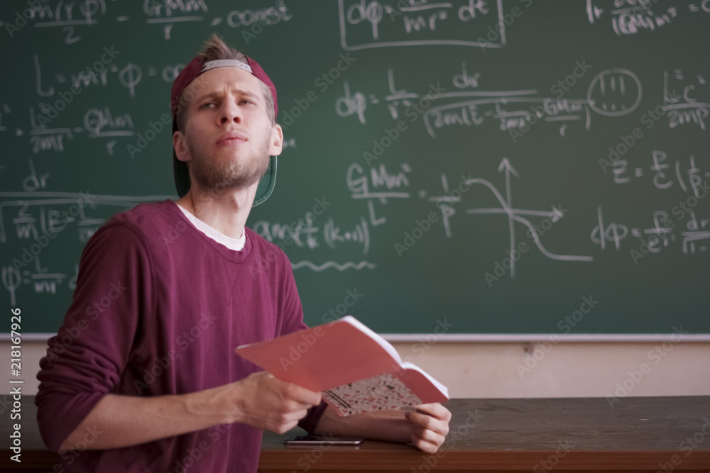 young student in casual standing near the blackboard with formulas and holding notebook with copy space young student in casual standing near the blackboard with formulas and holding notebook with copy space