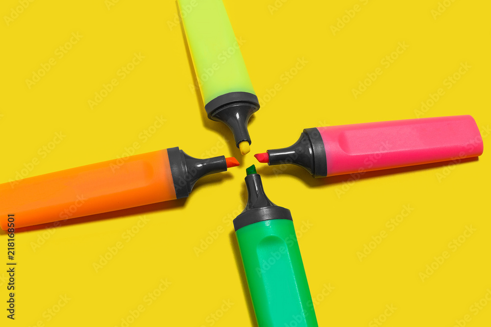 four new bright plastic marker lying on a yellow background with opened caps . concept of office supplies