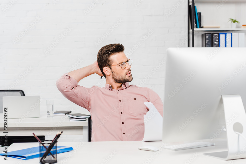 overworked young businessman stretching at modern office