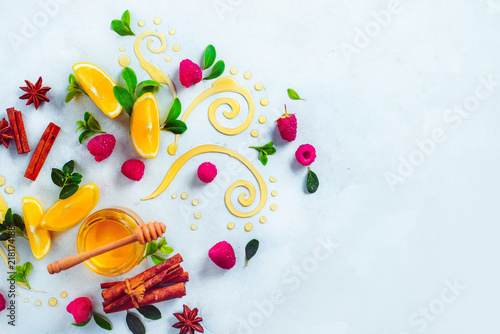 Honey dipper and honey in a jar on white background with berries, cinnamon and lemon slices. Decorative honey swirls. High key home remedies flat lay with copy space