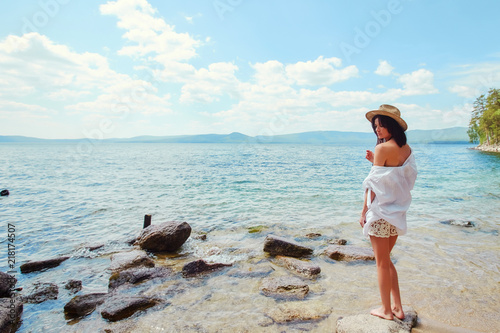 A slender woman in a white shirt and hat relaxes near the water photo