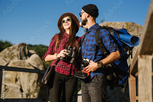 A couple traveling by the mountains wearing hipster clothes with backpack, vintage camera and binoculars