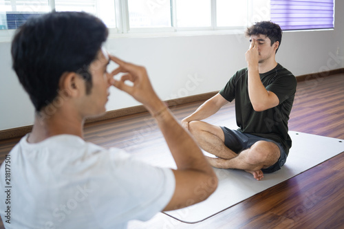 Man practicing alternate nostril breathing technique with personal instructor at yoga class. Guy sitting in sukhasana yoga pose. Pranayama concept.