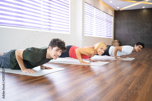 Smiling students doing four-limbed staff at class. Men and woman looking at camera and practicing yoga in gym. Yoga class concept.