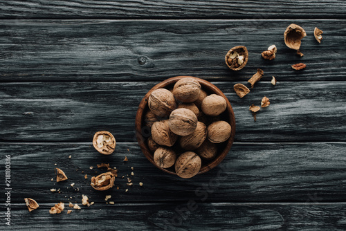walnuts in wooden bowl with nutshells on dark wooden table
