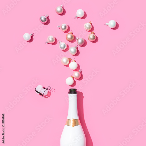 White champagne bottle with Christmas baubles decoration on pink background. Flat lay. Minimal party concept. © Zamurovic Brothers