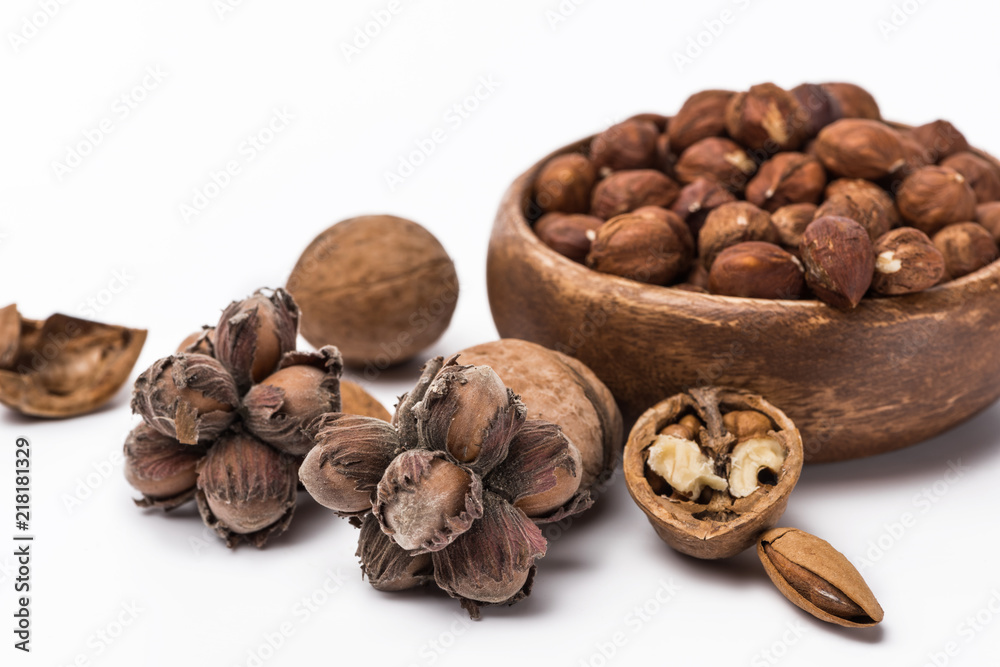 hazelnuts in wooden bowl near walnuts and almond isolated on white background