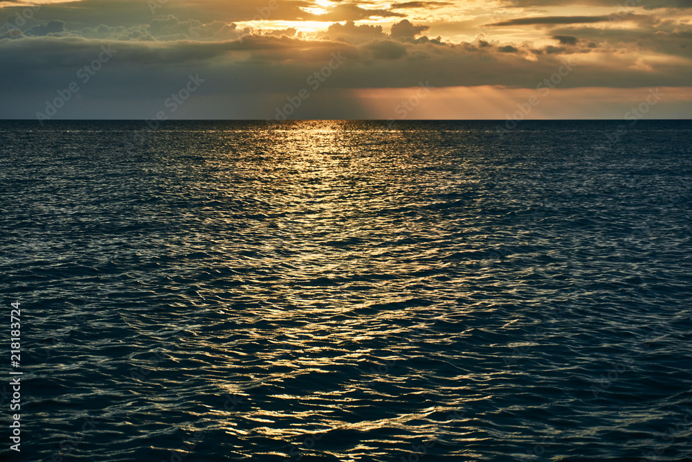 Obraz premium Beautiful bright orange sunset beyond the horizon line of the sea and reflection of the last rays on the surface of the water