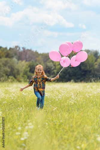 cheerful kid with pink balloons in hand running in meadow