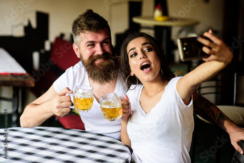 Couple cheerful mood drinking beer in pub. Couple in love on date drinks beer. Take selfie photo to remember great date in pub. Man bearded hipster and girl with beer glass full of craft beer