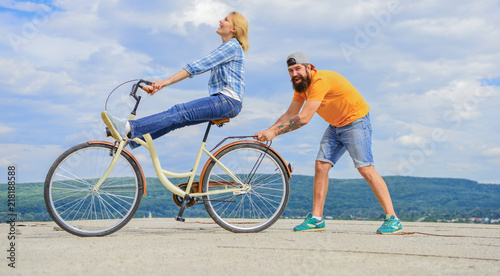 Learn cycling with support. Cycling technique. Woman rides bicycle sky background. Man helps keep balance and ride bike. How to learn to ride bike as adult. Girl cycling while boyfriend support her
