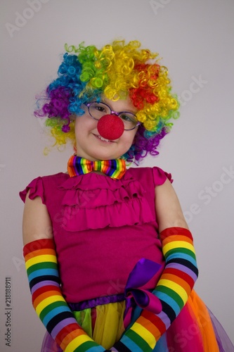 Little girl in clown costume.Little girl with glasses in colorful clown costume touches her red nose.