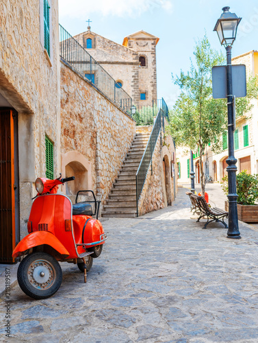 vintage red motor scooter parked on cobbled street in hostoric spanish village photo