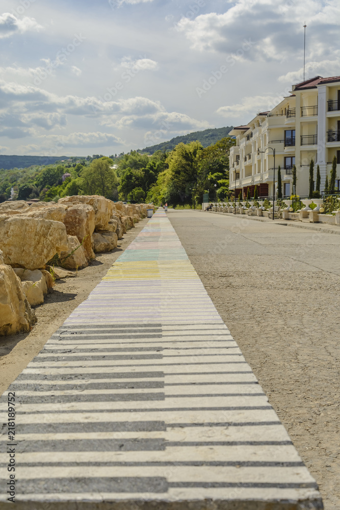 Walkway in the beach with hotel and a long bench with piano keys and a bright sky in Balchik, Bulgaria.