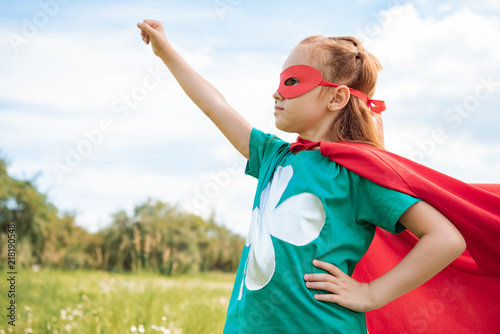 Fotografia adorable child in superhero costume with outstretched arm in summer field