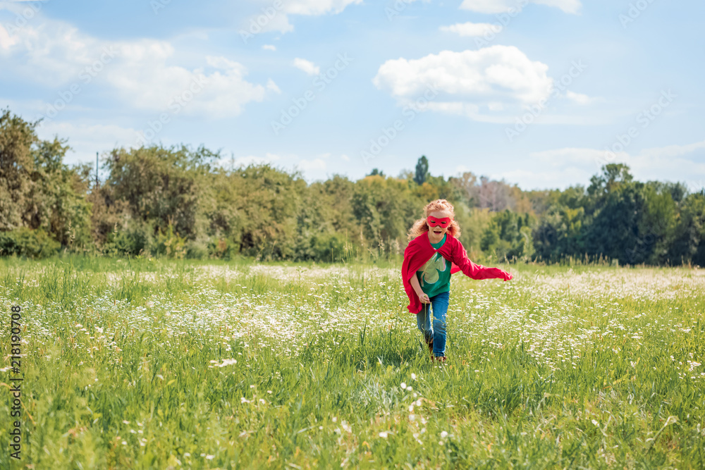 little kid in red superhero costume running in meadow on summer day little kid in red superhero costume running in meadow on summer day
