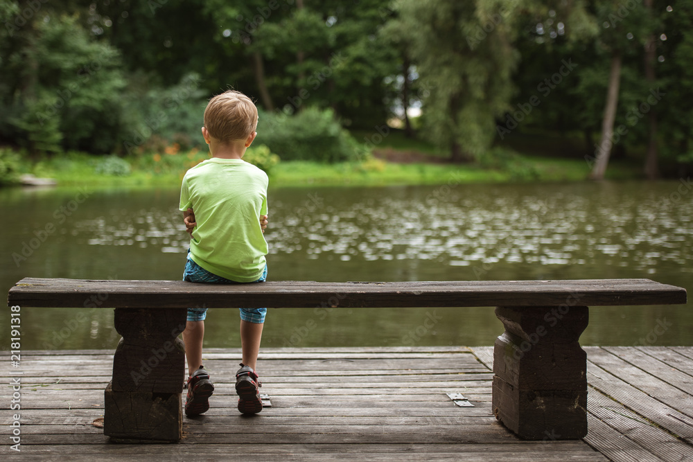 Small boy sit back on the wooden bench by the lake. Stock Photo | Adobe  Stock