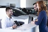 Smiling professional car dealer showing offer to happy buyers