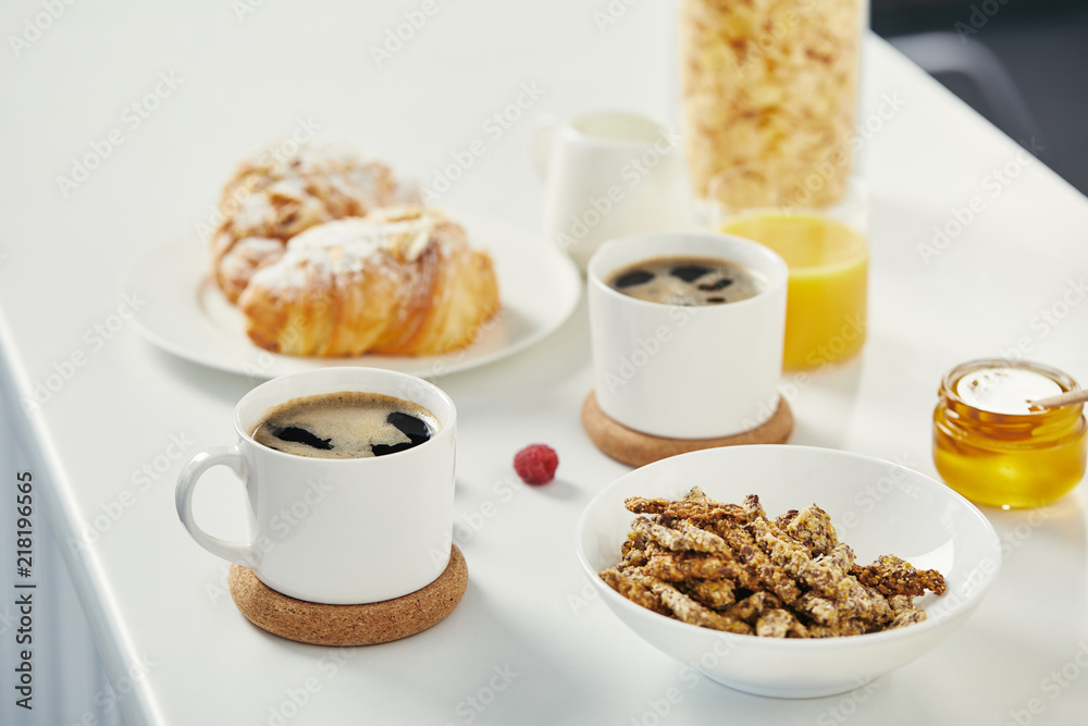 close up view of cups of coffee, honey and croissants for breakfast on white surface close up view of cups of coffee, honey and croissants for breakfast on white surface