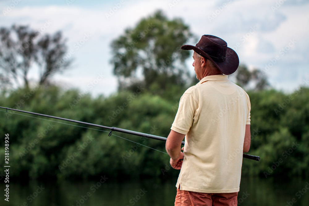 A fisherman in shorts and hat is fishing on the shore of the lake. Fishing, recreation A fisherman in shorts and hat is fishing on the shore of the lake. Fishing, recreation