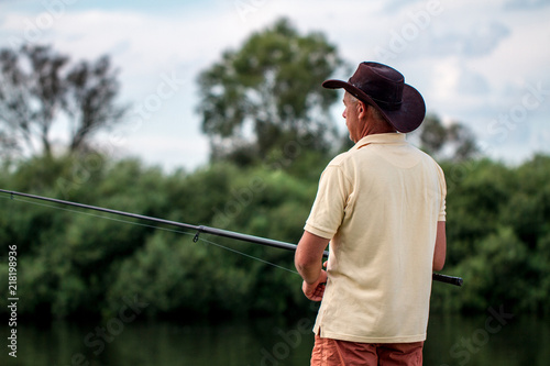 A fisherman in shorts and hat is fishing on the shore of the lake. Fishing, recreation