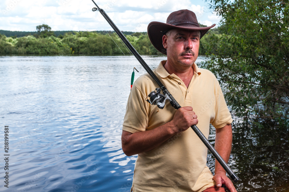Portrait of a fisherman with a fishing rod on his shoulder on the  background of the lake. Fishing. Fishing gear Stock Photo