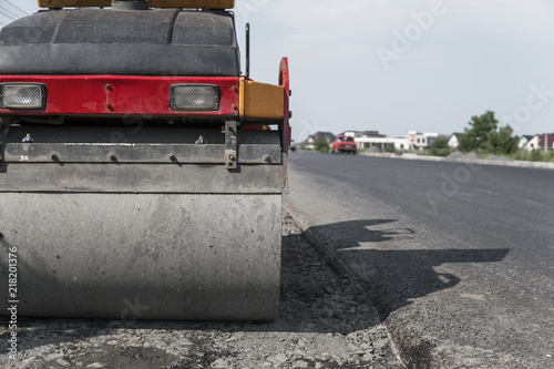 Orange Vibration roller compactor standing on a ground near asphalts road at road construction and repairing asphalt pavement works with a blue sky. photo