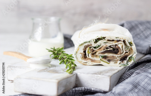 Rolls with mushroom, cukes and cream cheese served with cream and rosemary on white wooden cutting board. Thin Armenian pita bread or lavash. Snack.