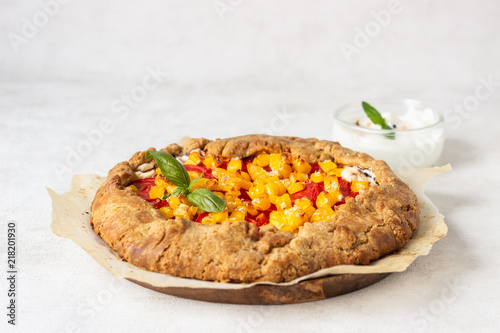 Homemade rustic open pie (galette) with tomato and sweet corn with fresh basil and greek yogurt on white background.