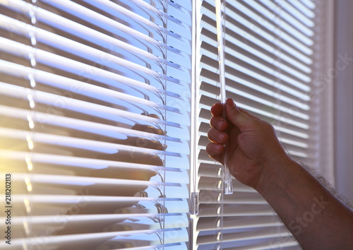 Man's hand closes the horizontal blinds on the Windows.