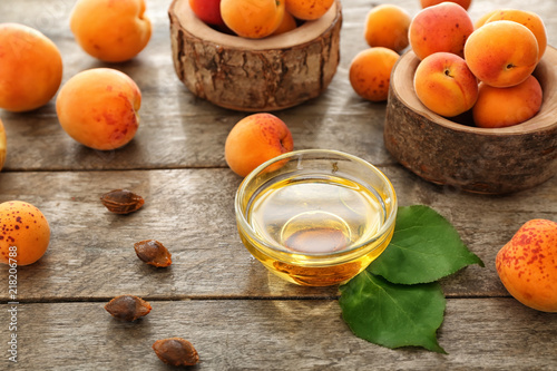 Bowl with essential oil and fresh apricots on wooden table