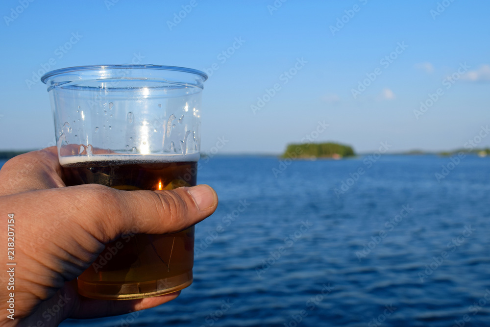 Hand holding a beer on summer day. Beautiful lake landscape on background. Hand holding a beer on summer day. Beautiful lake landscape on background.