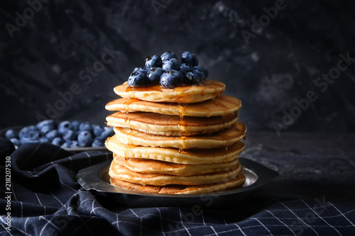 Plate with tasty pancakes and blueberries on dark table