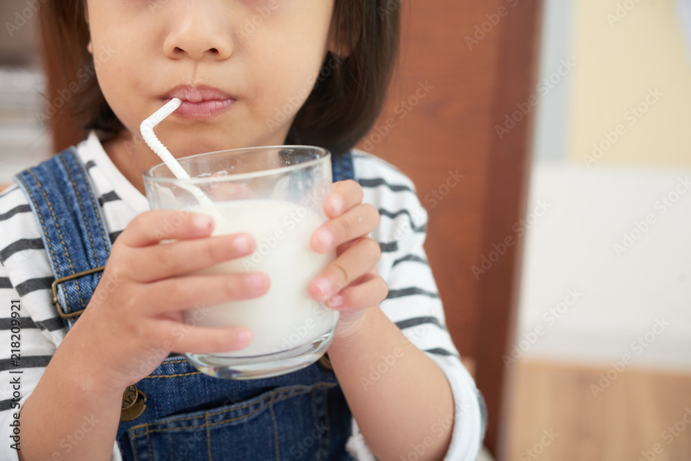 Crop shot of little casual girl having glass of milk and drinking with straw at home Crop shot of little casual girl having glass of milk and drinking with straw at home