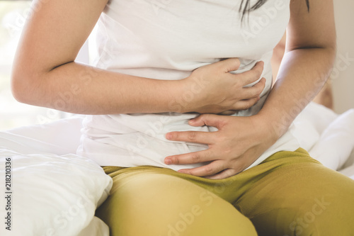 Asian young woman suffering from abdominal pain while sitting on bed at home