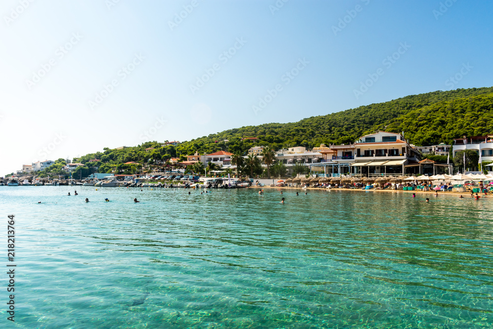 The shoreline of a Greek island with buildings, beaches and people in the water, peaceful, and relaxing