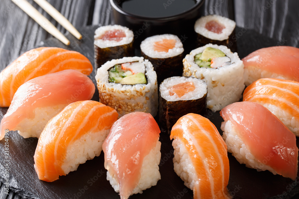 Freshly prepared sushi with salmon and tuna, California rolls, maki with soy sauce, chopsticks close-up on black slate board. horizontal Freshly prepared sushi with salmon and tuna, California rolls, maki with soy sauce, chopsticks close-up on black slate board. horizontal