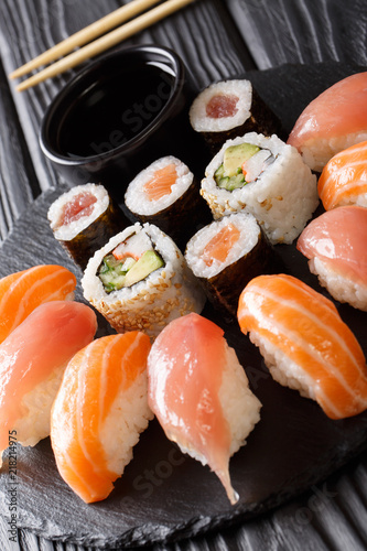 Set of sushi with salmon and tuna, California rolls, maki, soy sauce closeup on a black slate board. vertical