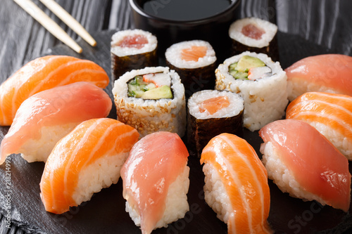 Freshly prepared sushi with salmon and tuna, California rolls, maki with soy sauce, chopsticks close-up on black slate board. horizontal