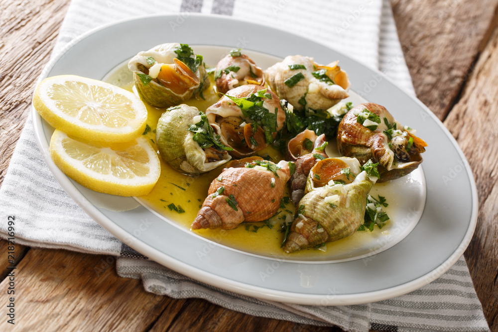 French recipe Whelks with a sauce of butter, garlic and parsley, lemon close-up. horizontal