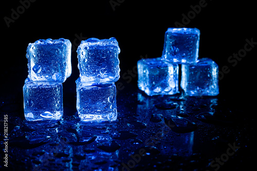 Blue ice cubes reflection on black table background.